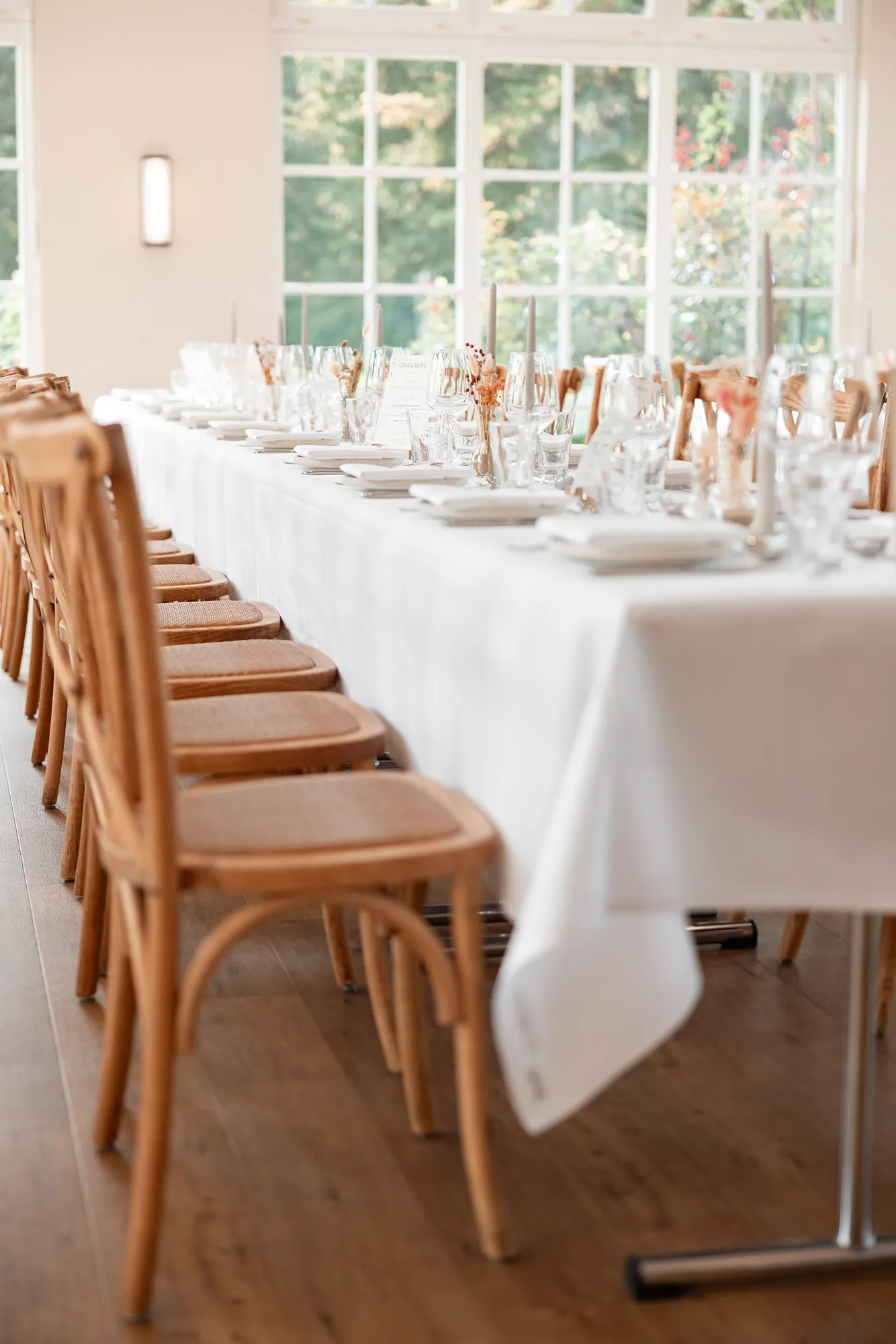 Lange, festlich gedeckte Tafel in der Orangerie mit Holzstühlen