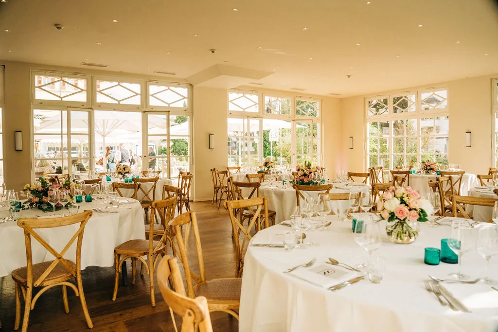 Orangerie mit festlich gedeckten runden Tischen und Blumenschmuck