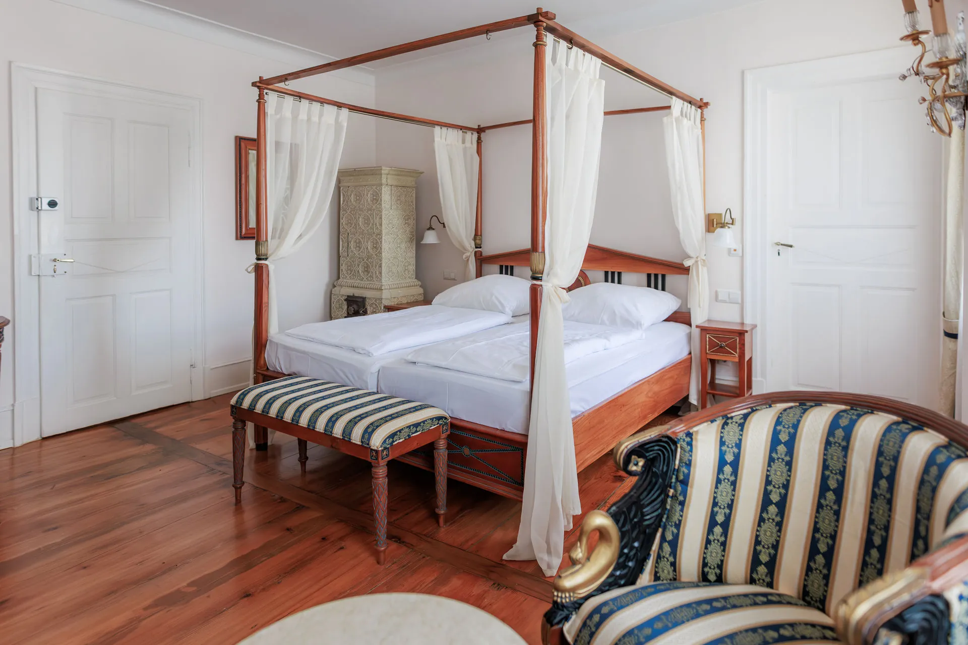 Himmelbett mit gestreifter Bank und Biedermeiersessel im Schlosszimmer