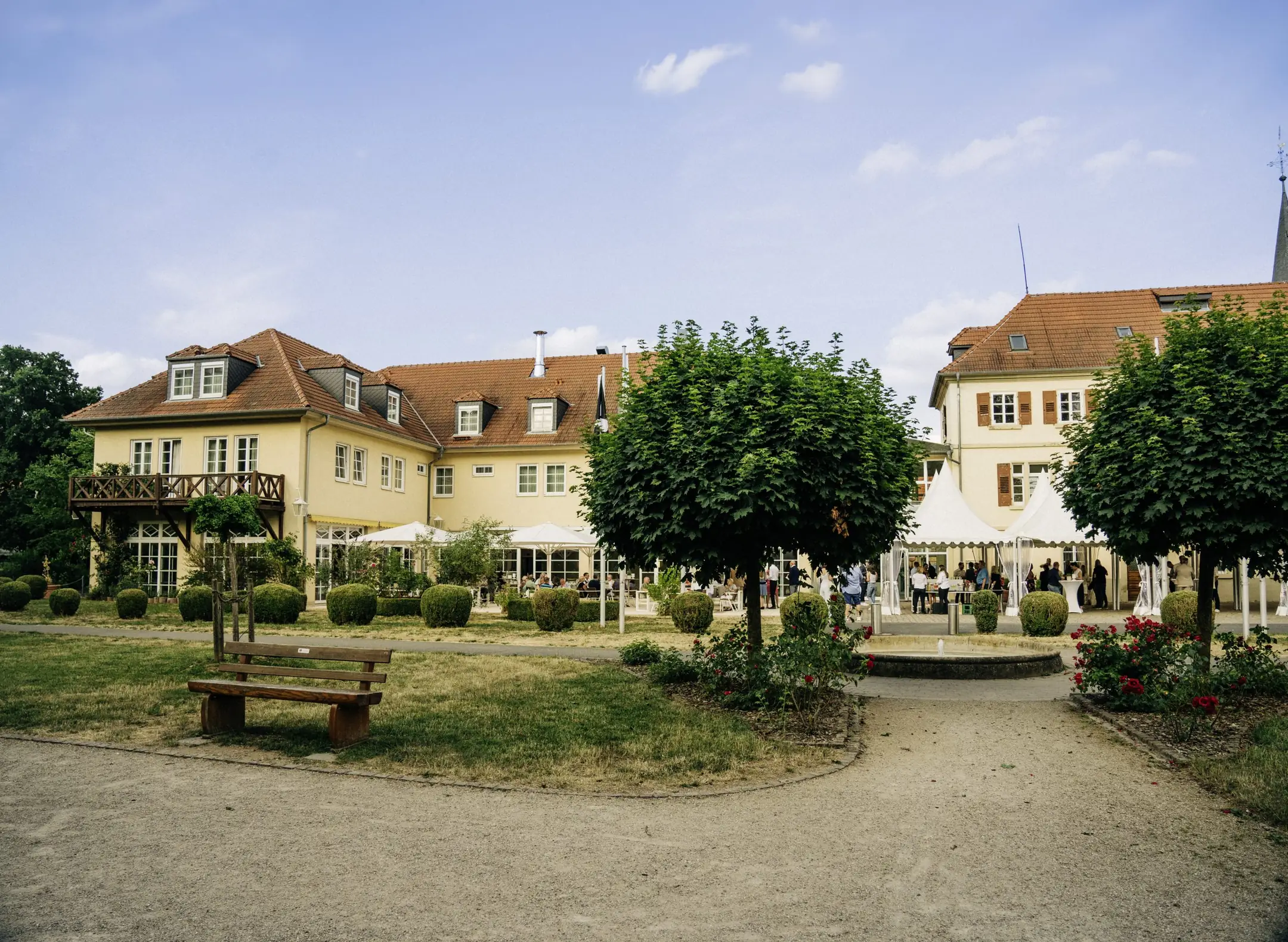 Schlosshotel Neckarbischofsheim mit Innenhof, Bäumen und Parkbank an einem Sommertag