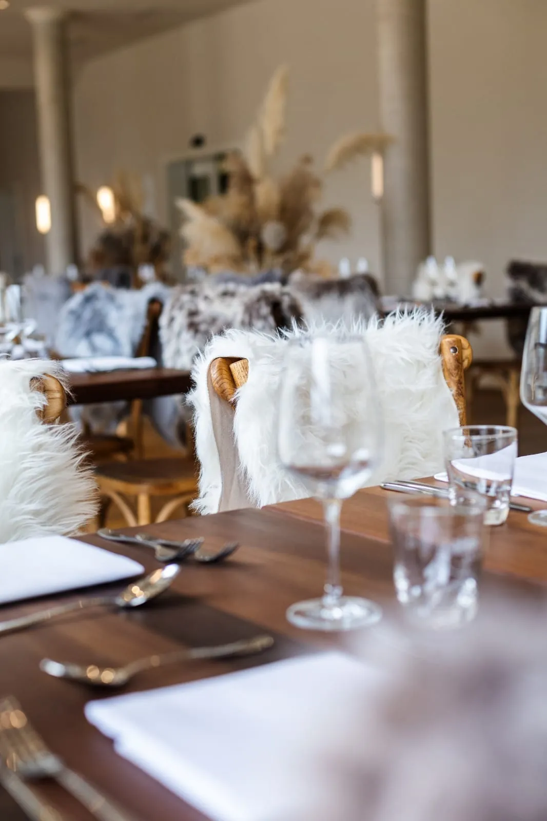 Gedeckter Tisch mit Weingläsern und fellbezogenen Stühlen
