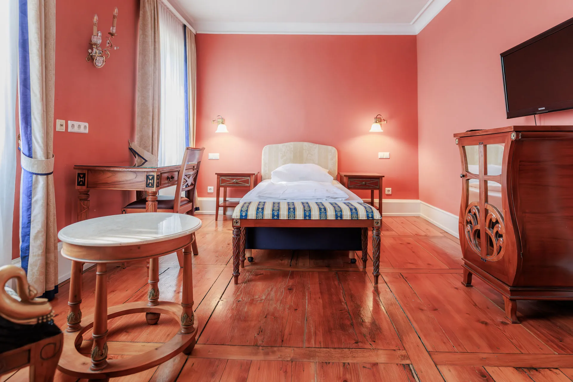 Einzelzimmer mit roter Wand, Einzelbett, Dielenboden und Marmortisch