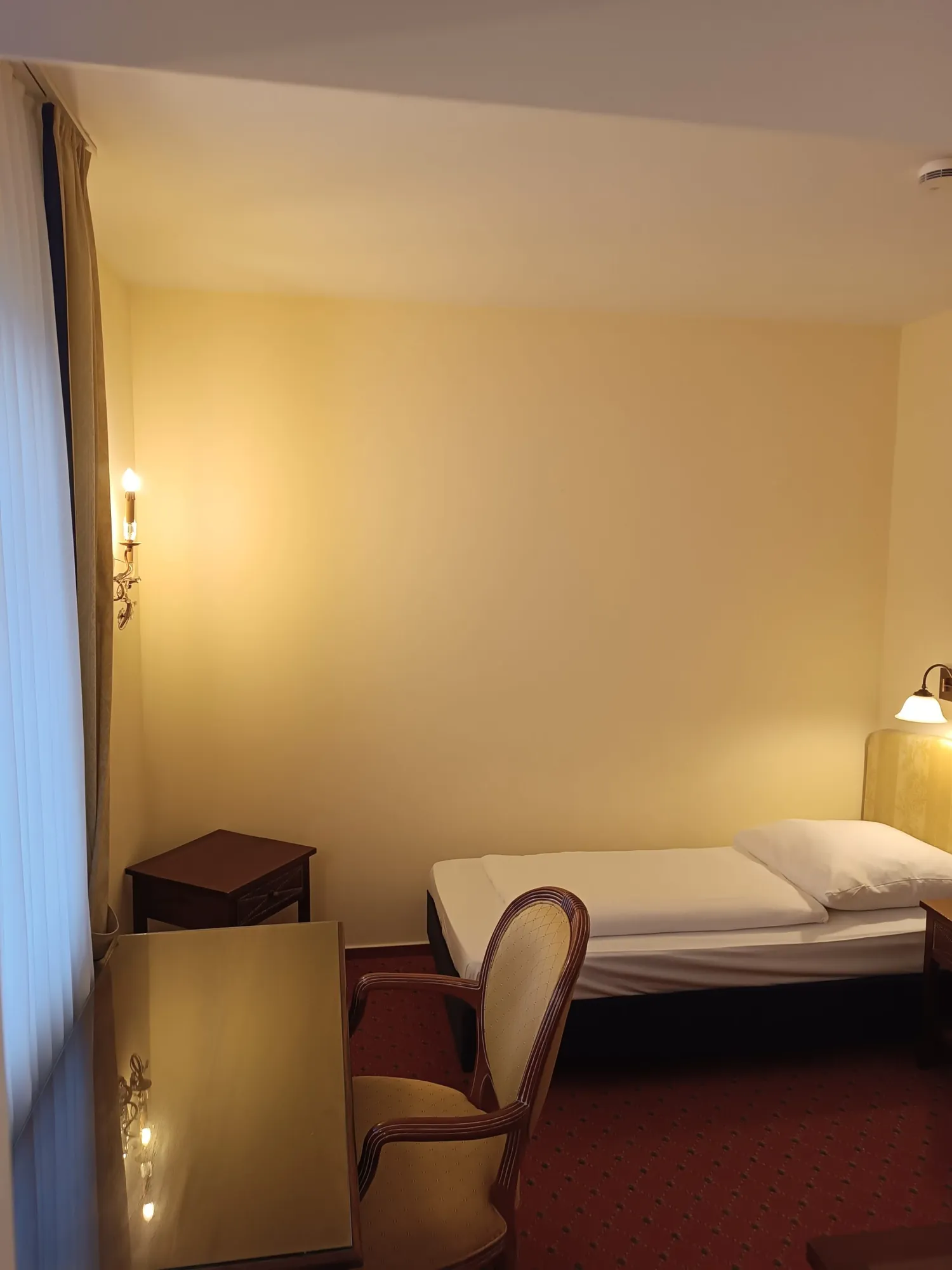 Schlichtes Einzelzimmer mit Einzelbett, Stuhl und rotem Teppich
