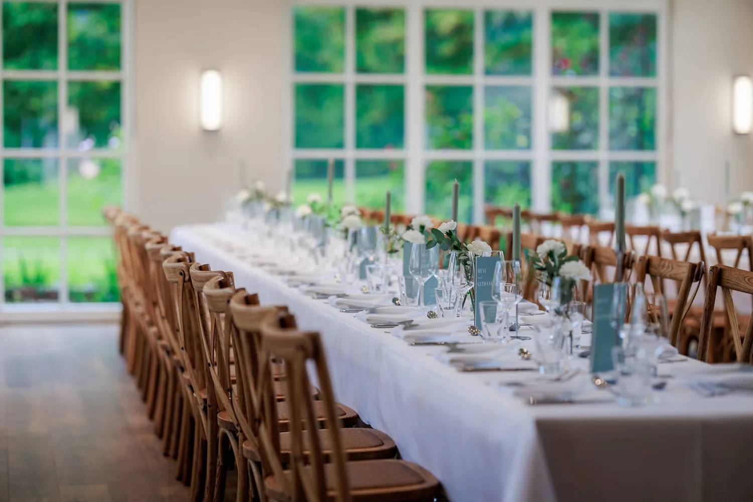 Lange Festtafel mit Holzstühlen und Blumen vor der Fensterfront