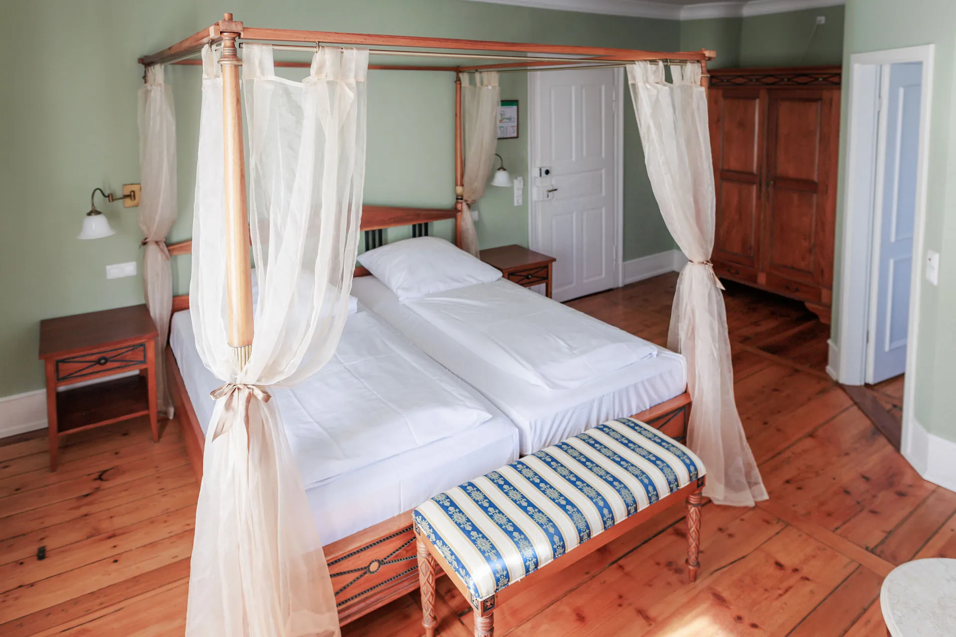 Himmelbett mit Tüllvorhängen und gestreifter Bank im grünen Schlosszimmer