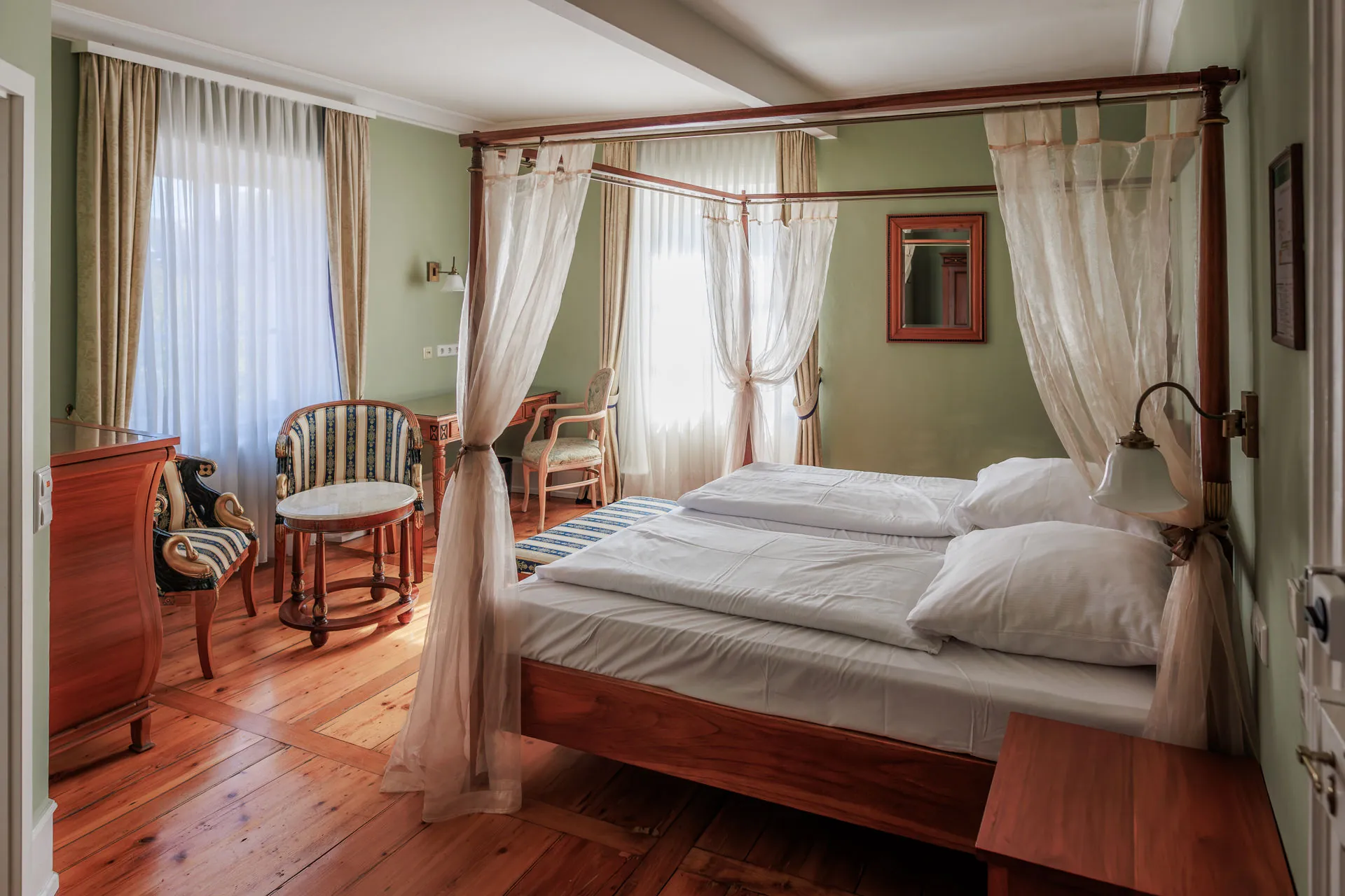 Schloss-Doppelzimmer mit grünen Wänden, Himmelbett und Sitzecke am Fenster