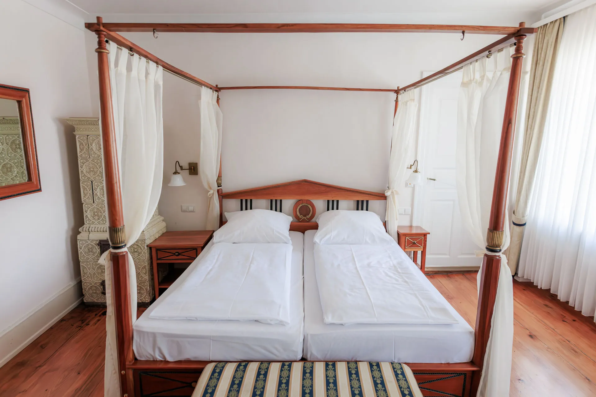 Schloss-Doppelzimmer mit Himmelbett, weißen Vorhängen und Kachelofen