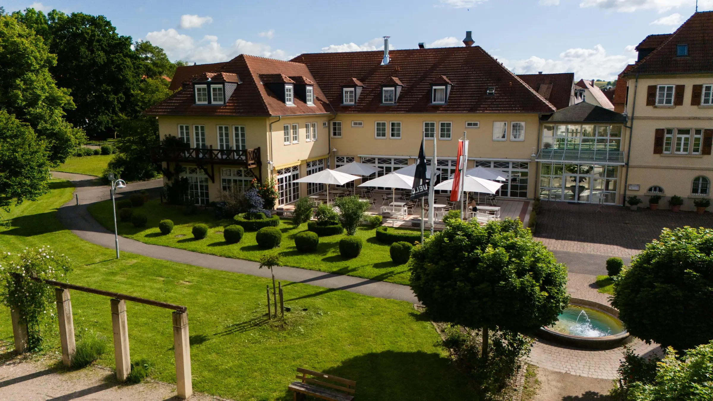 Schlosshotel mit Terrasse, Buchsbaumgarten und Brunnen aus erhöhter Perspektive im Sommer